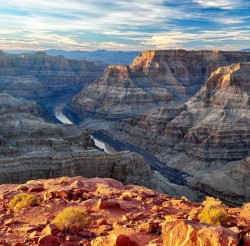 The vast plateaus of the Grand Canyon stretch for miles and a river runs through at the base.